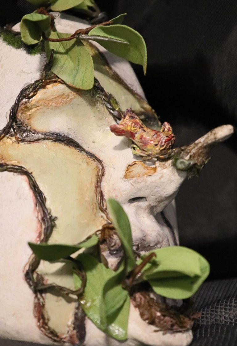 Frontal view of the 'Forest Bird Mother' sculpture with a colorful bird on the nose and leaves at the mouth


