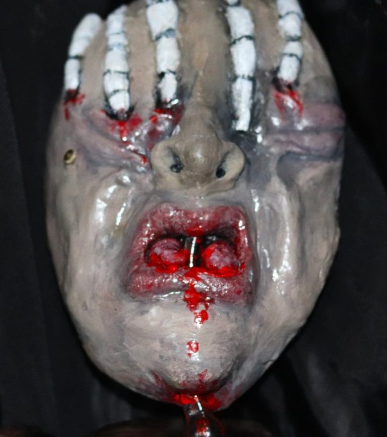 Front view of “SPLIT” sculpture – real bike lever and skeletal hand Front view of “SPLIT” mask sculpture with split tongue, bike brake lever, and skeletal hand detail