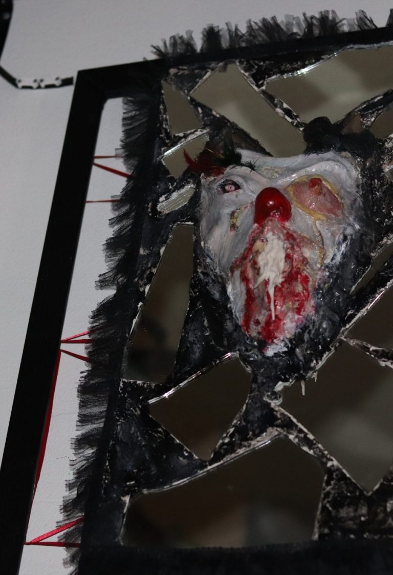 Full view of “Vagina Mouth” sculpture by Maskuindo, displayed inside black frame, featuring broken mirror glass and embedded sculptural mask